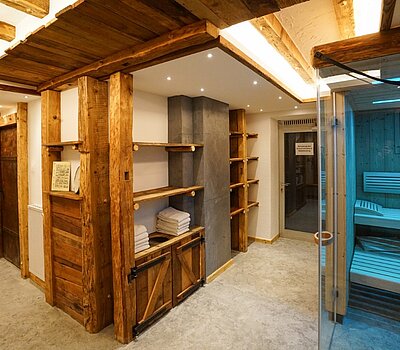 Wellnessbereich mit Wänden und Decken aus Holz, offenen Regalen und einer modernen Sauna mit Glasfront.